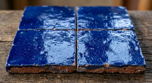 Four cobalt blue square tiles with glossy textured surfaces and irregular clay edges