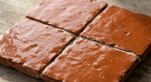 Four clay pink square tiles with reflective textured surfaces and irregular edges